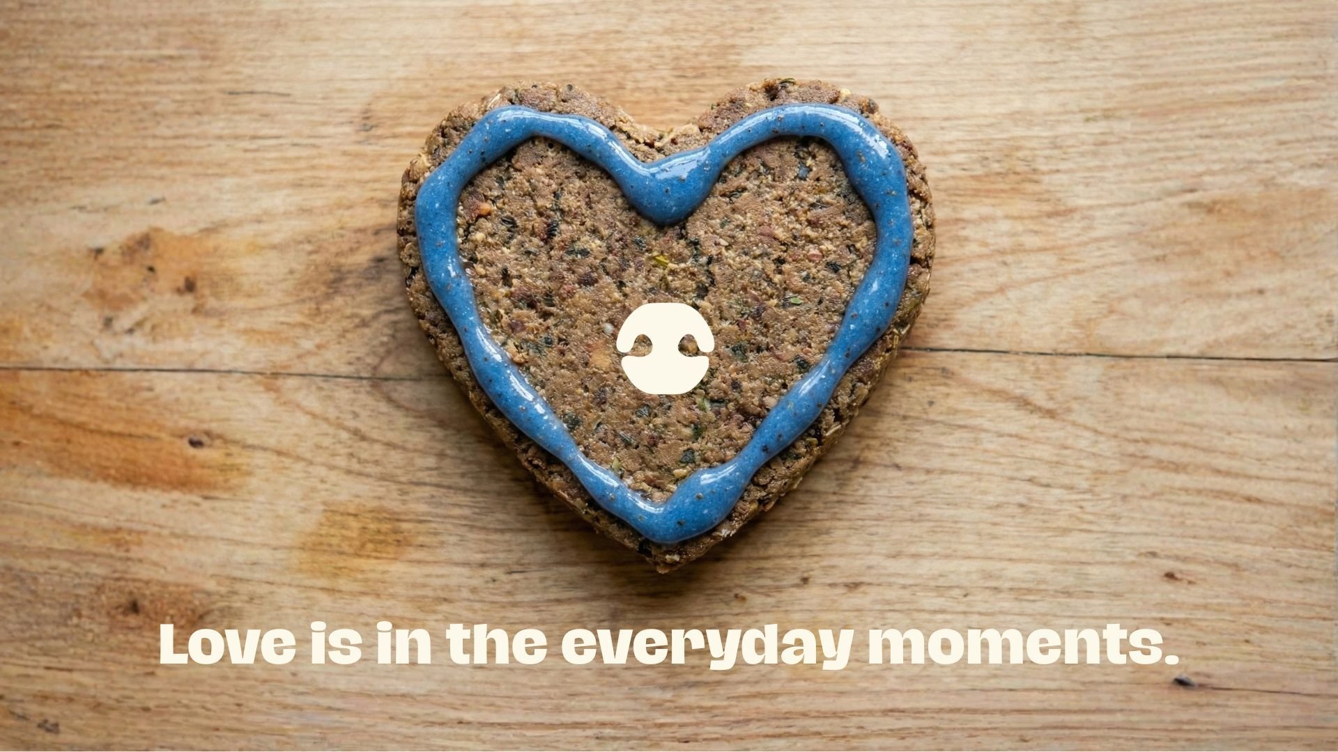 Heart-shaped dog wunderdog patty with blue topper on a wooden surface with the text “Love is in the everyday moments.”