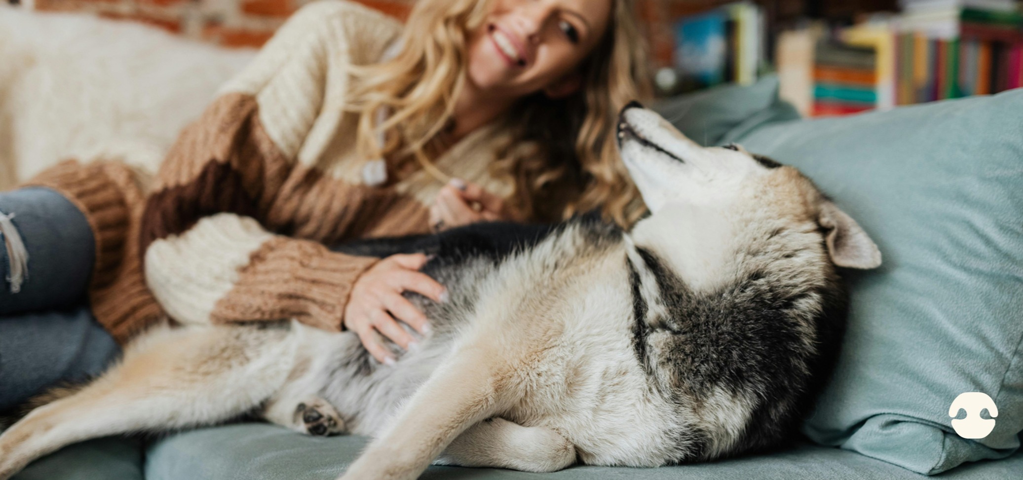 Woman relaxing on a sofa at home while cuddling a Siberian Husky dog, showing calm bonding and comfort in a cosy indoor setting.
