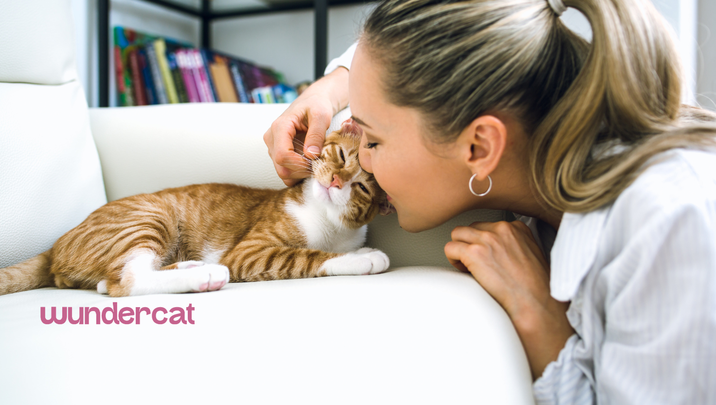 Woman cuddling and kissing an orange tabby cat resting on a white sofa at home.