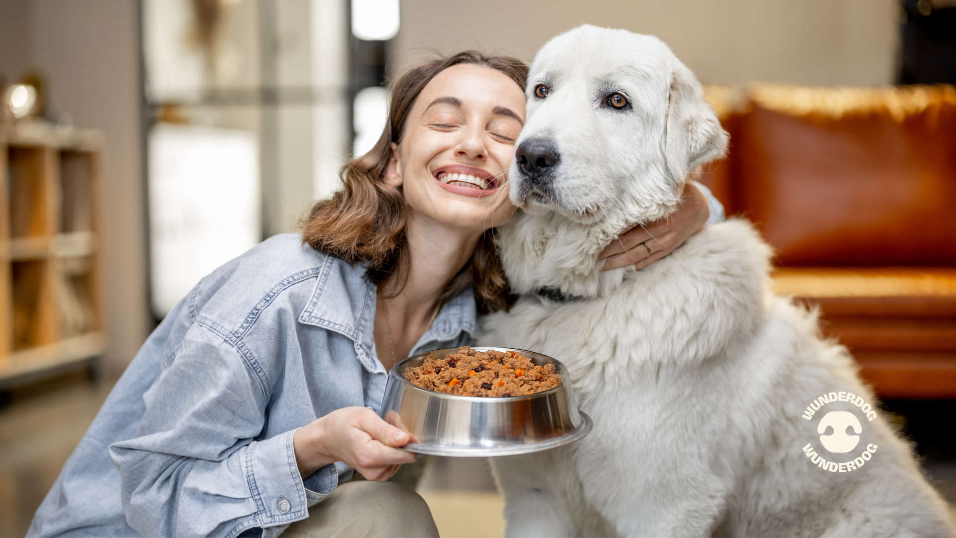 Happy woman hugging her large white dog while holding a bowl of Wunderdog fresh dog food, showcasing the bond between pets and healthy nutrition at home.