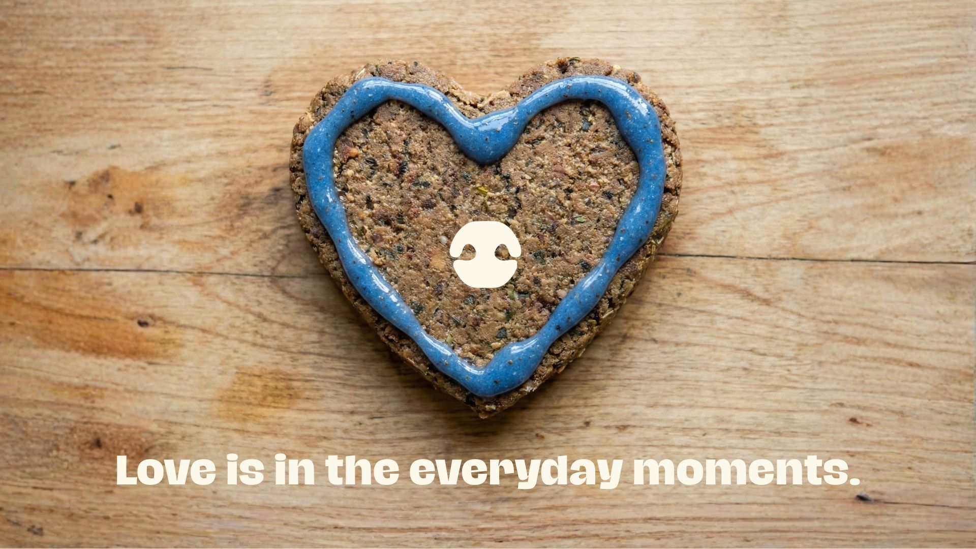 Heart-shaped dog wunderdog patty with blue topper on a wooden surface with the text “Love is in the everyday moments.”